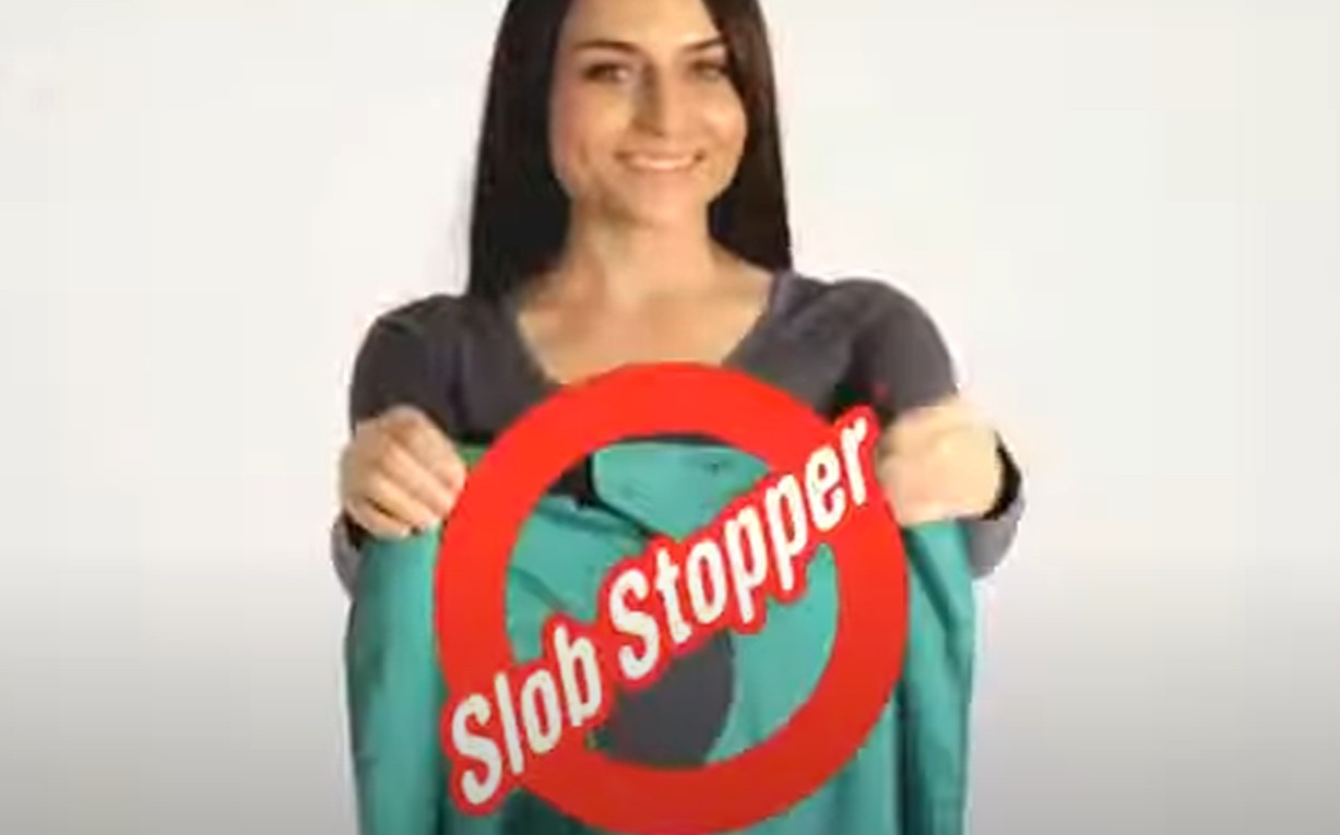 A woman smiling while holding up a teal Slob Stopper adult bib